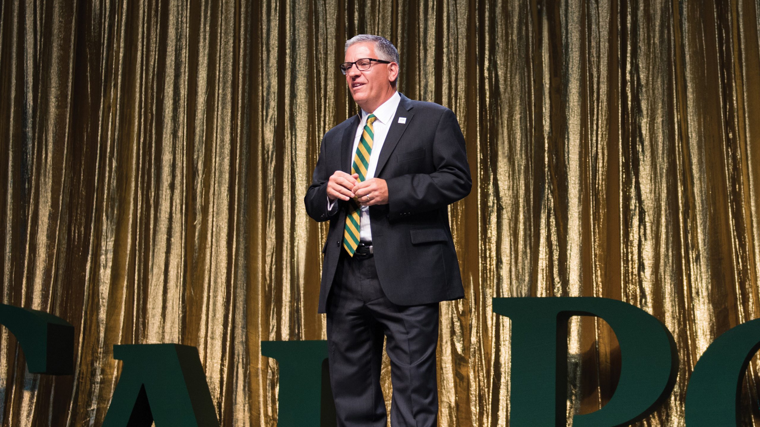 President Armstrong speaks on stage at the Evening of Green and Gold with a Cal Poly sign in the background