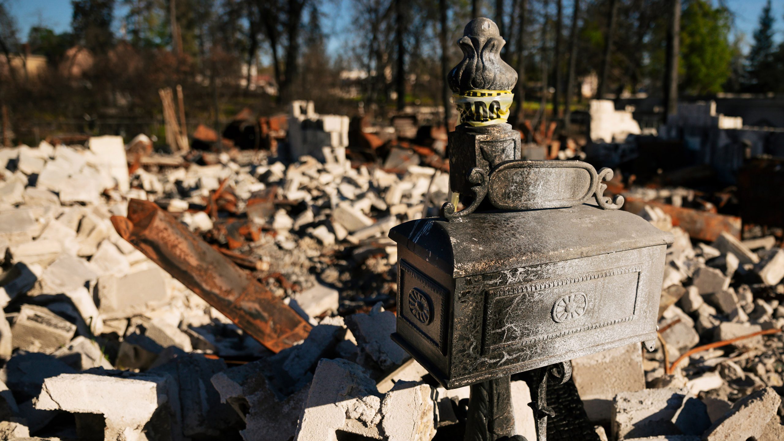 A blistered mailbox stands with a destroyed house in the background in Paradise, CA. Photo by Joe Johnston.