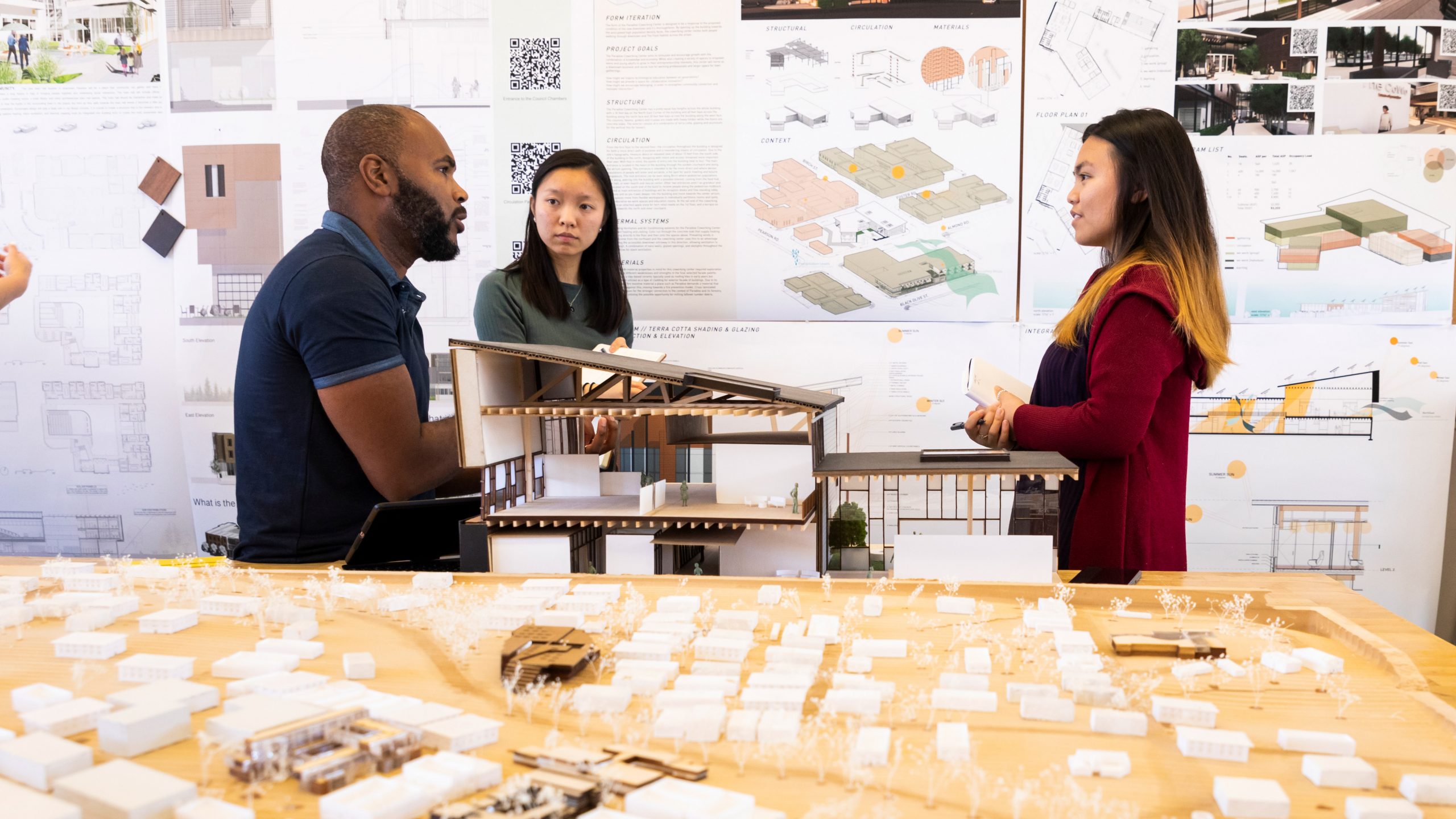 Faculty member Jermaine Washington speaks with two architecture students in front of their final design poster. Photo by Joe Johnston.