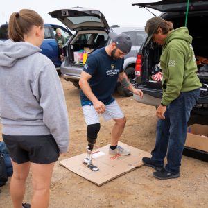 Kyle Kelly tries on his prosthetic ankle on the beach in Morro Bay with Cal Poly engineering students.