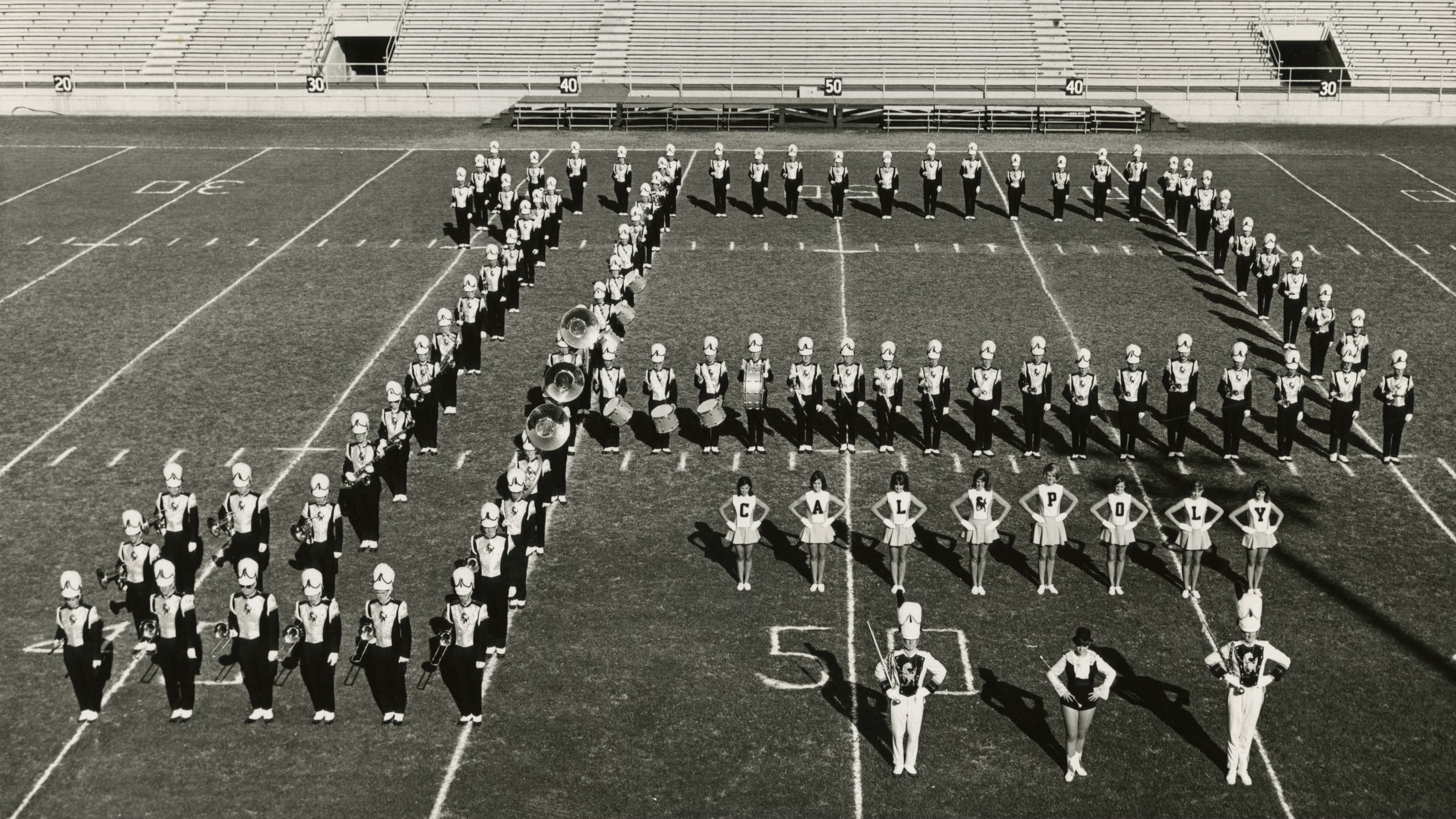 The marching band stands in the shape of a 'P' in the football stadium with majorettes and drum majors.