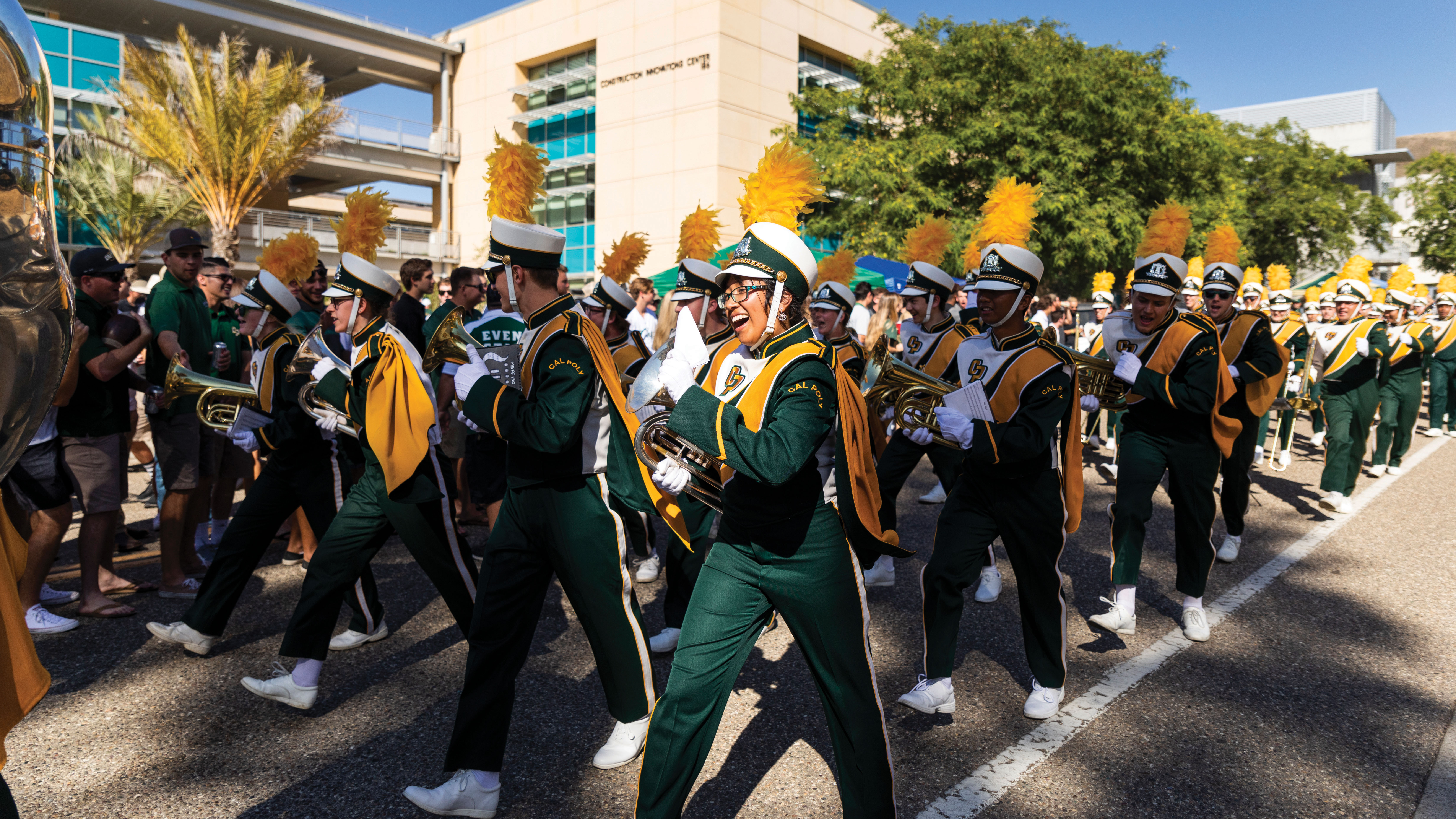 Musicians march while smiling and holding their instruments on Cal Poly's campus.