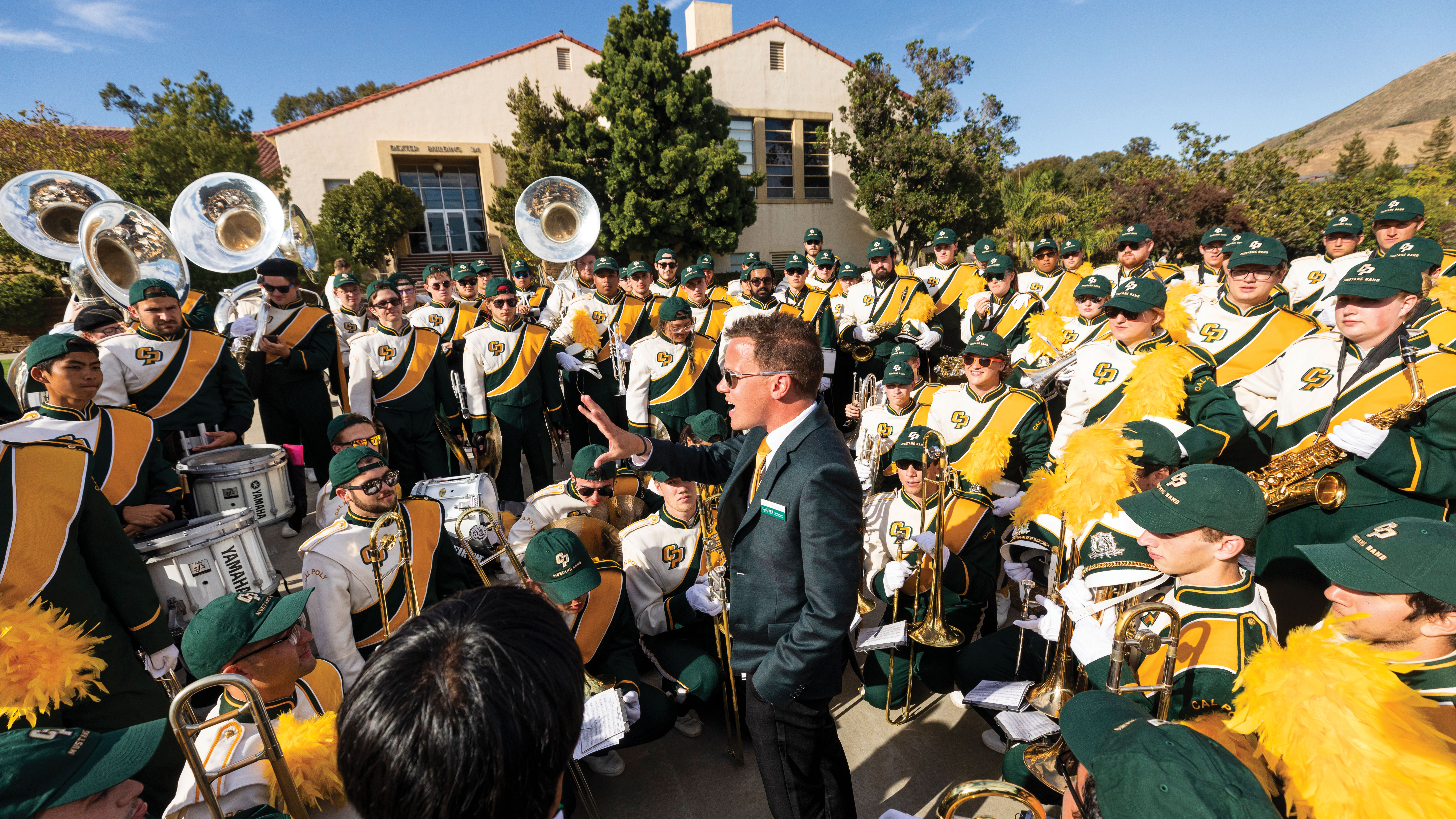 Associate Director of Bands Nick Waldron make a speech surrounded by the Mustang Band on Cal Poly's campus.