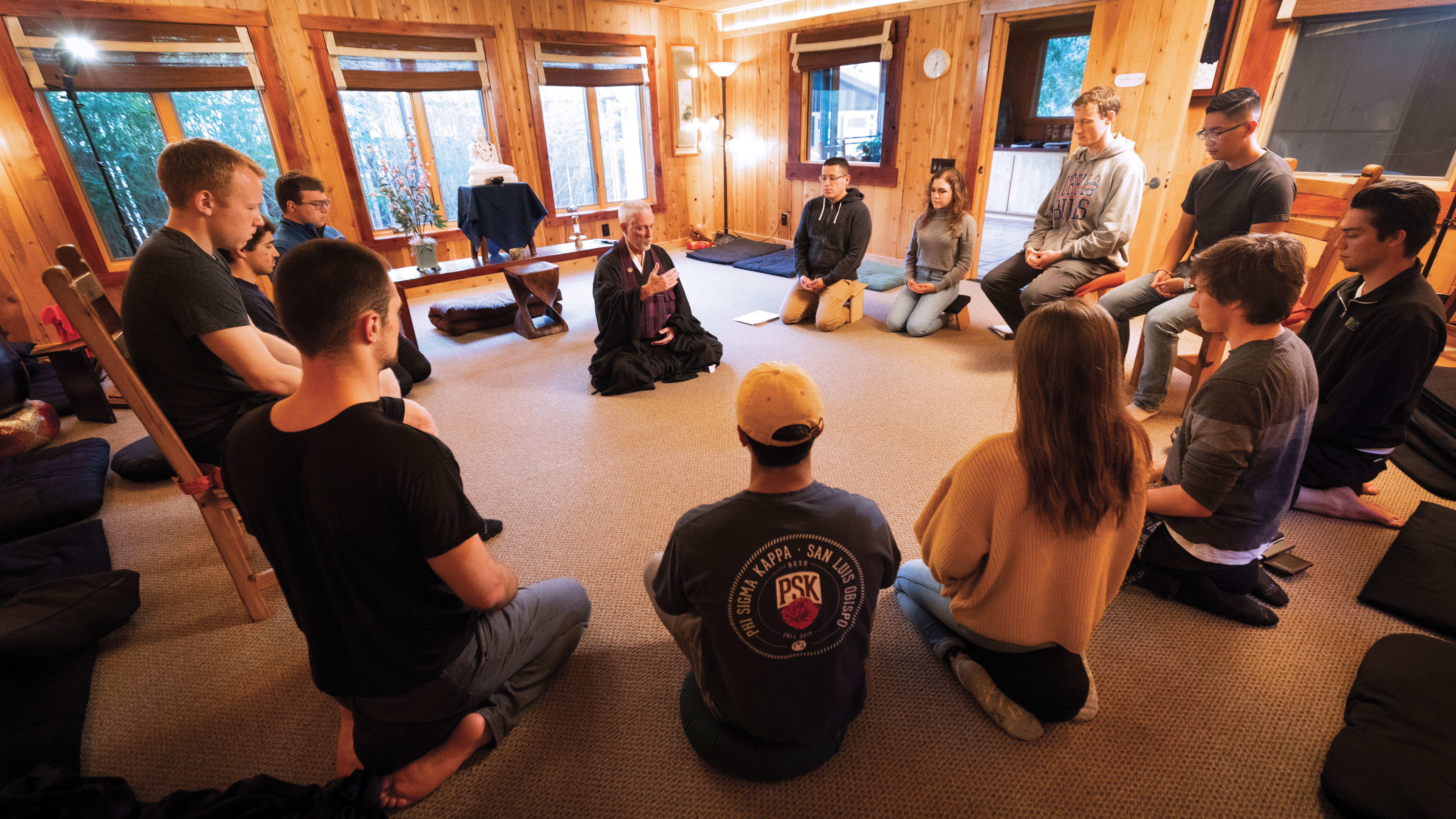 Students sit in a circle with their eyes closed around a zen priest.