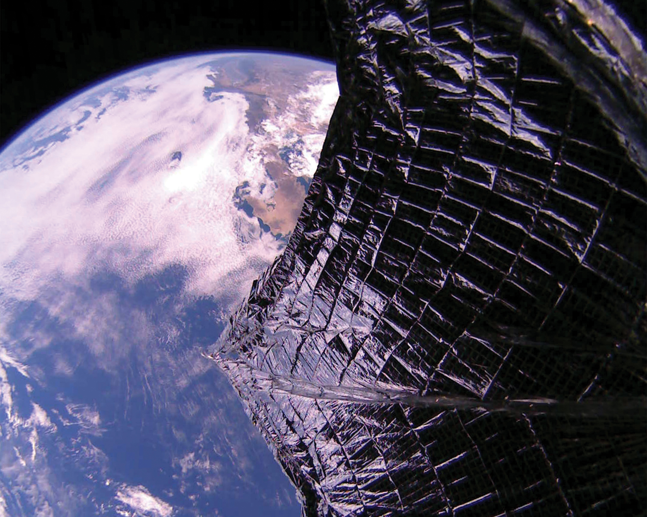 From space, a wide metal foil sail partially obscures the view of the Earth.