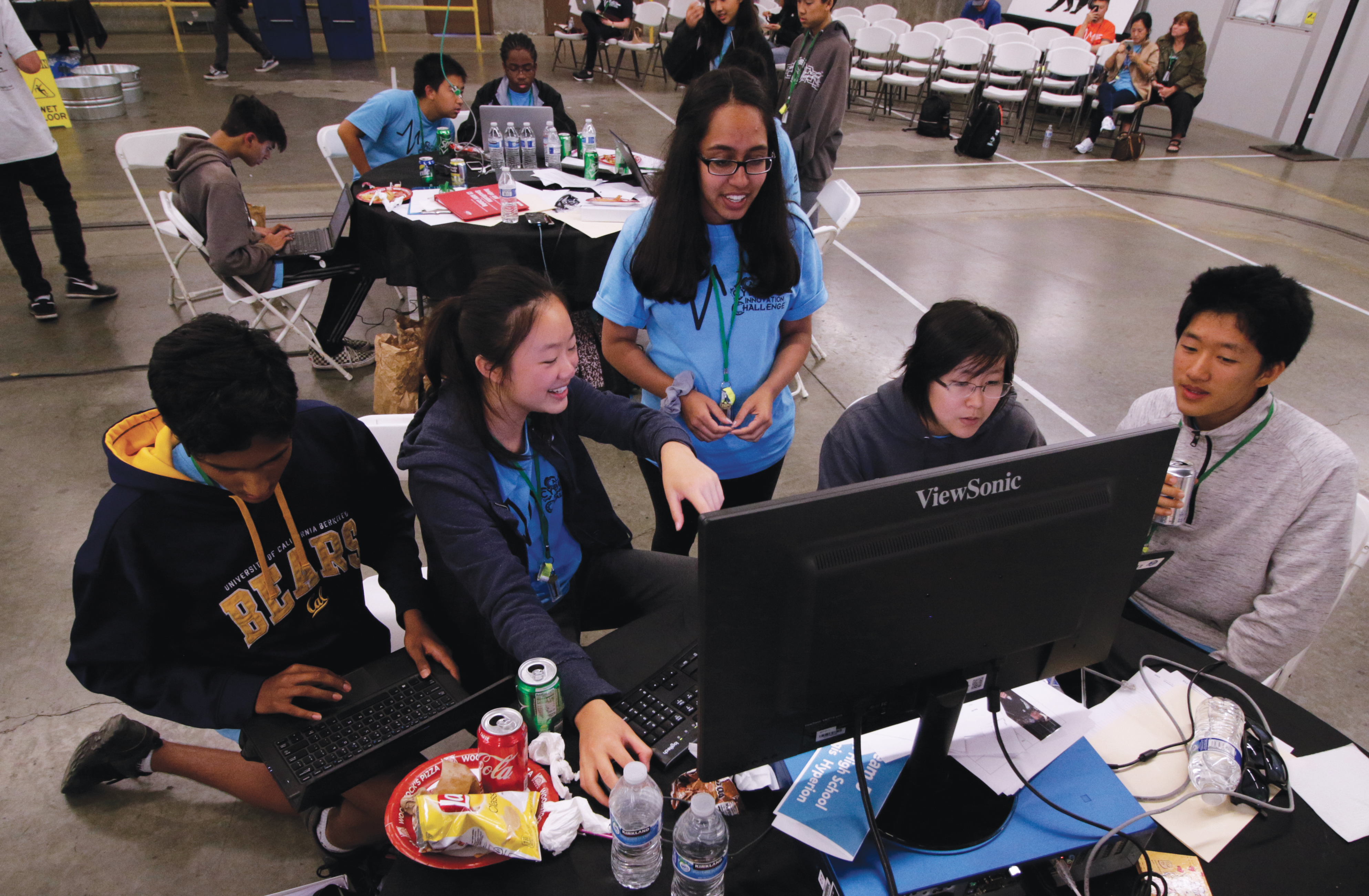 A group of teens gathers around a computer at Cal Poly, working together with empty snack and drink containers on the desk.