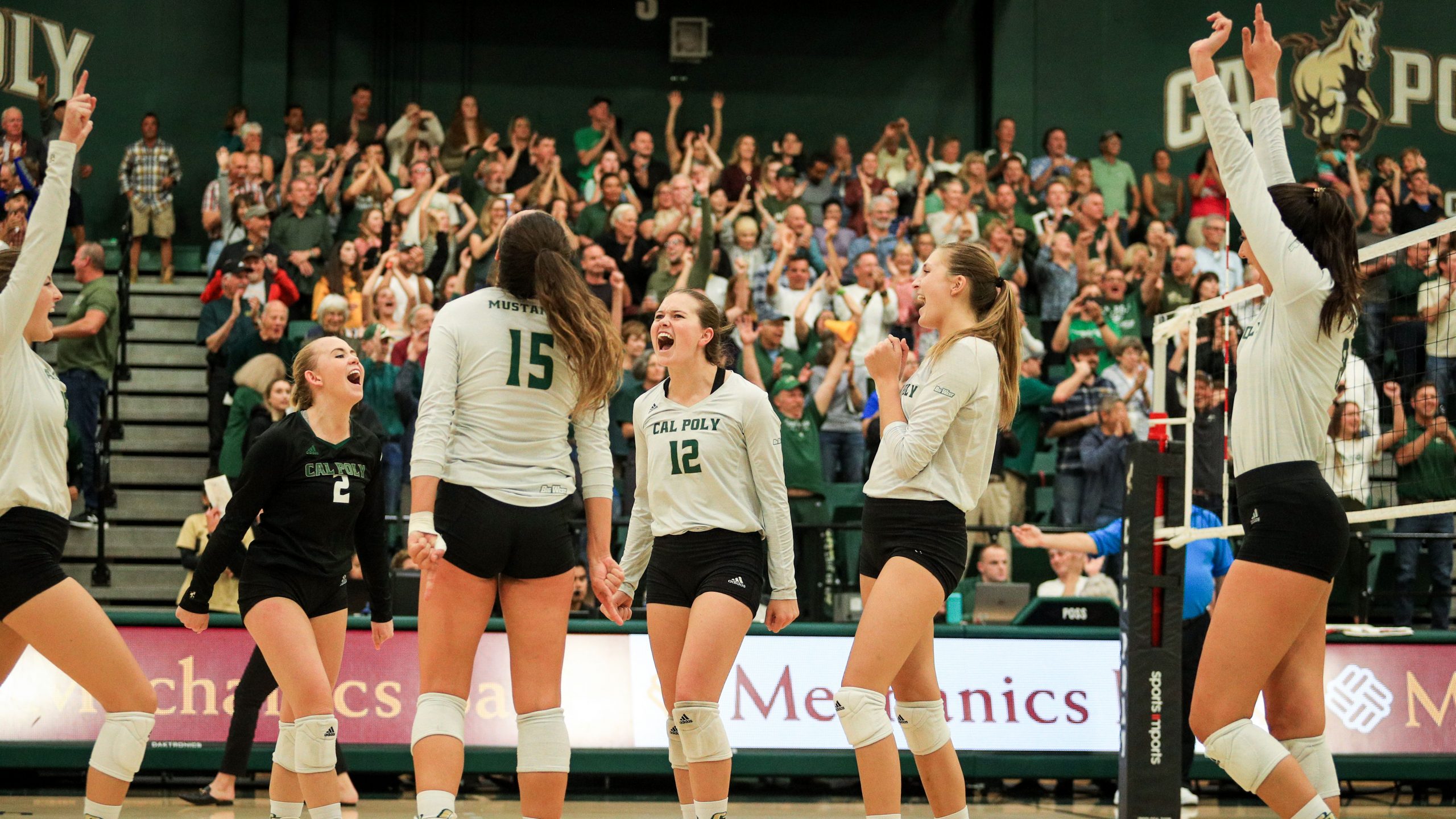 Athletes on Cal Poly's volleyball team celebrate a point in front of a crowd at Mott Athletic Center