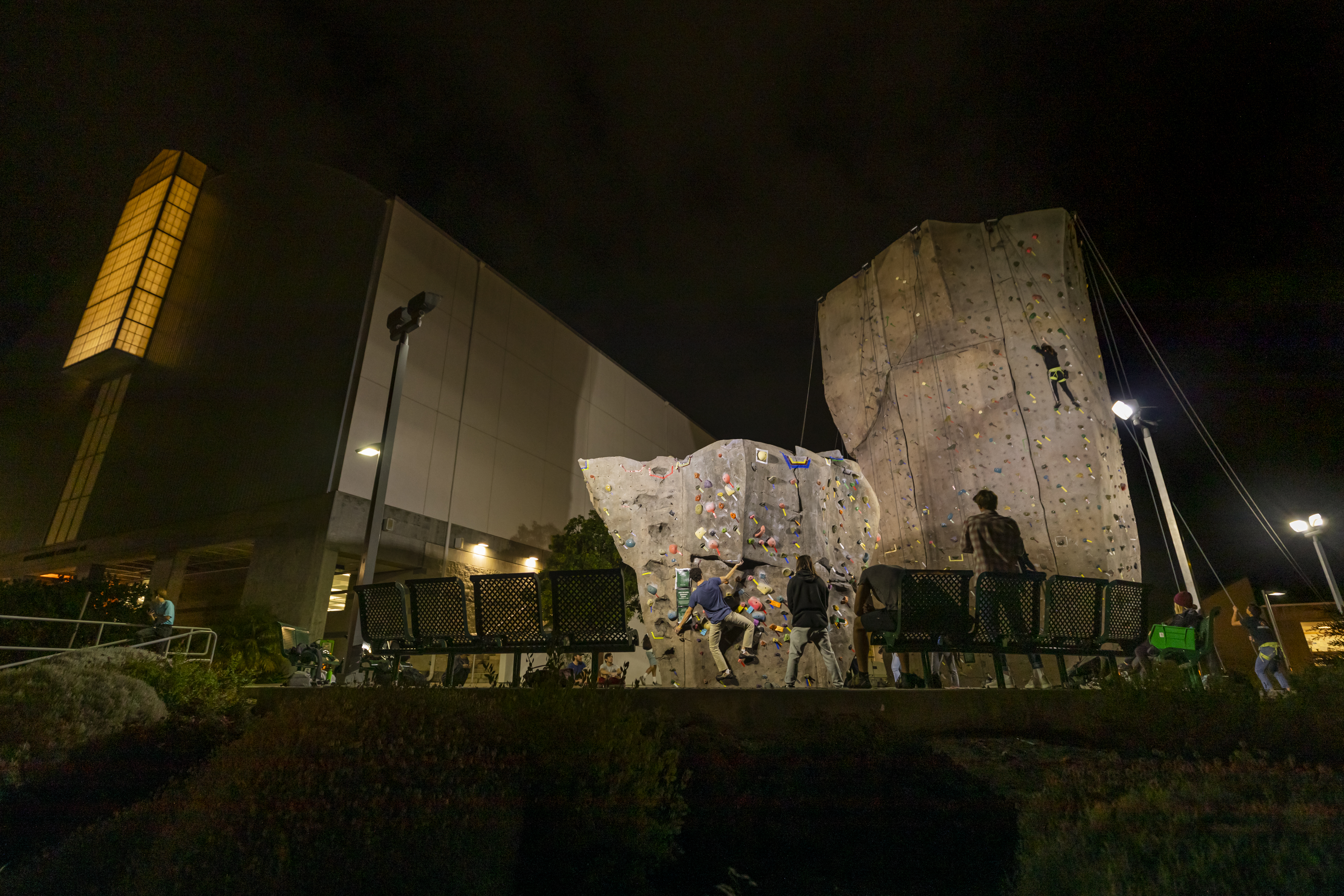 Students climb on the university's rock climbing park at night.