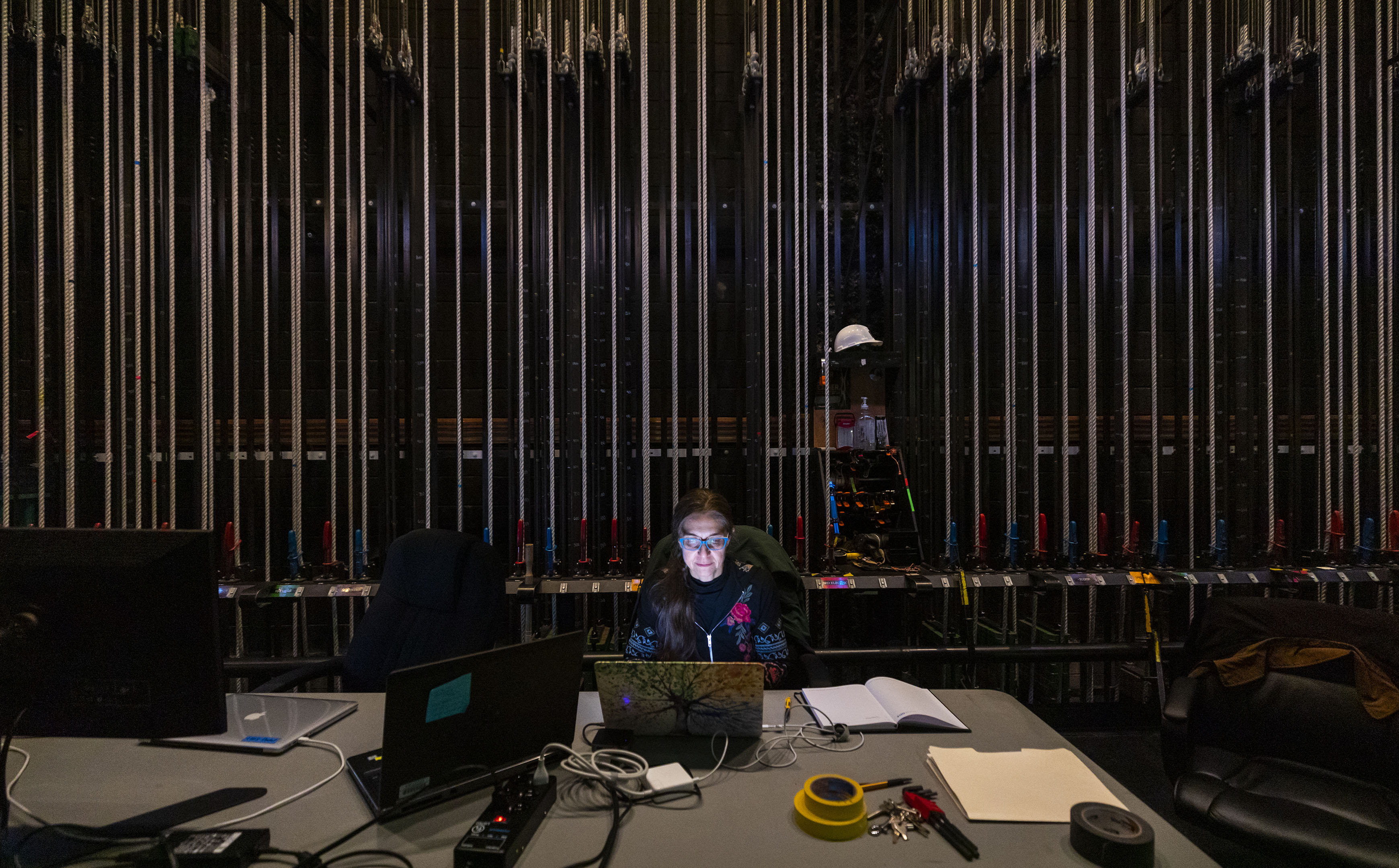 A woman sits in front of a laptop, notes and keys in the wings of the Performing Arts Center stage