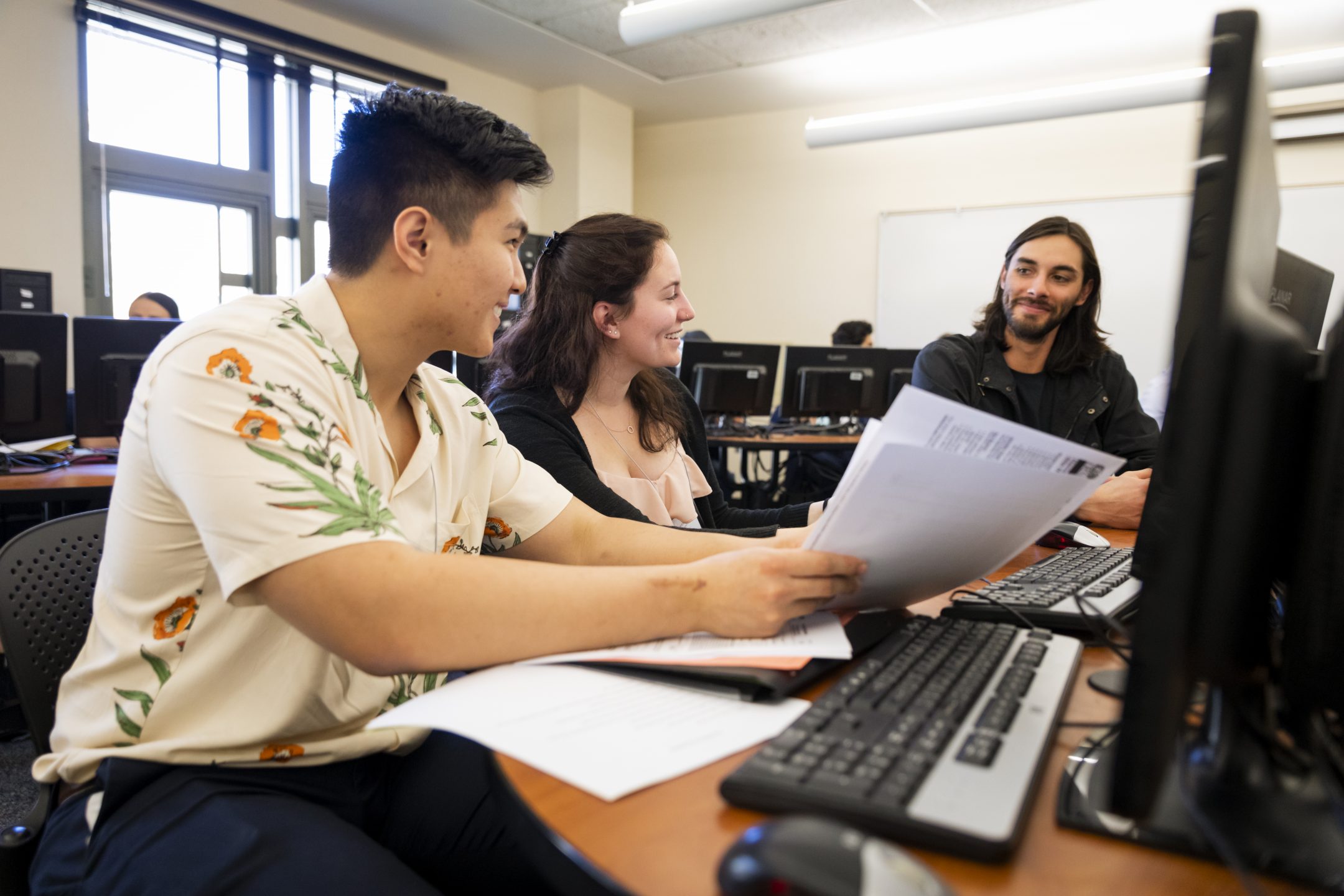 Two students sit at a desk reviewing tax forms with a young man.