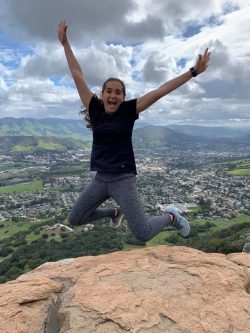 A young woman leaps into the air at the top of a mountain overlooking San Luis Obispo