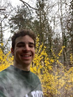 A young man in a Cal Poly t-shirt hikes among trees and yellow flowers.