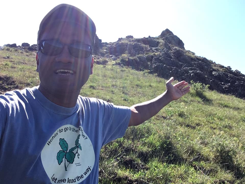 Rajakaruna, in a baseball cap and sunglasses, in a selfie taken on a sunlit hillside