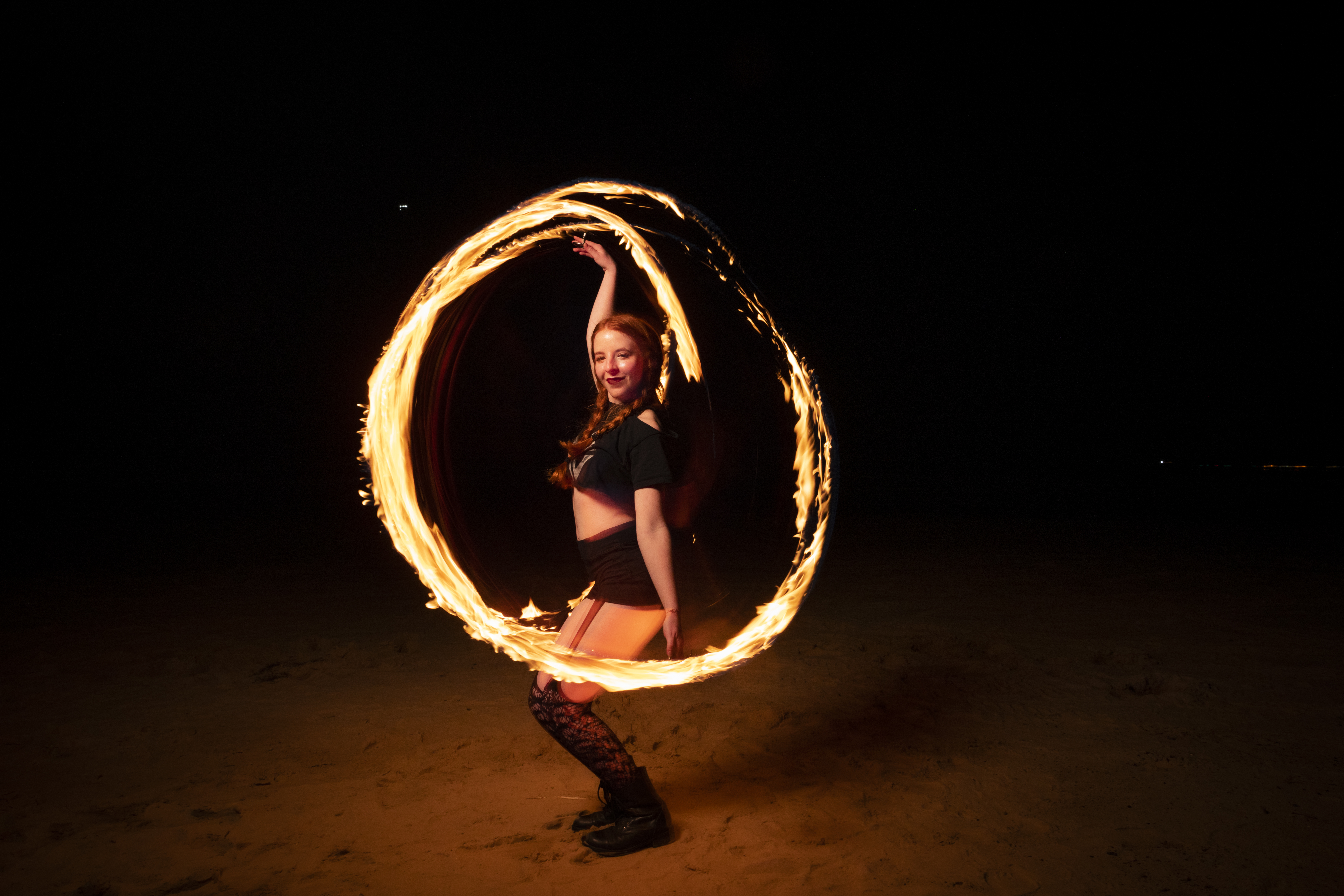 A young woman stands on the sand illuminated by an apparent ring of fire.