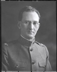 A man in glasses and a military uniform poses for a black and white bust portrait