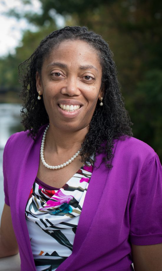 A woman in a purple top smiles in an outdoor portrait.