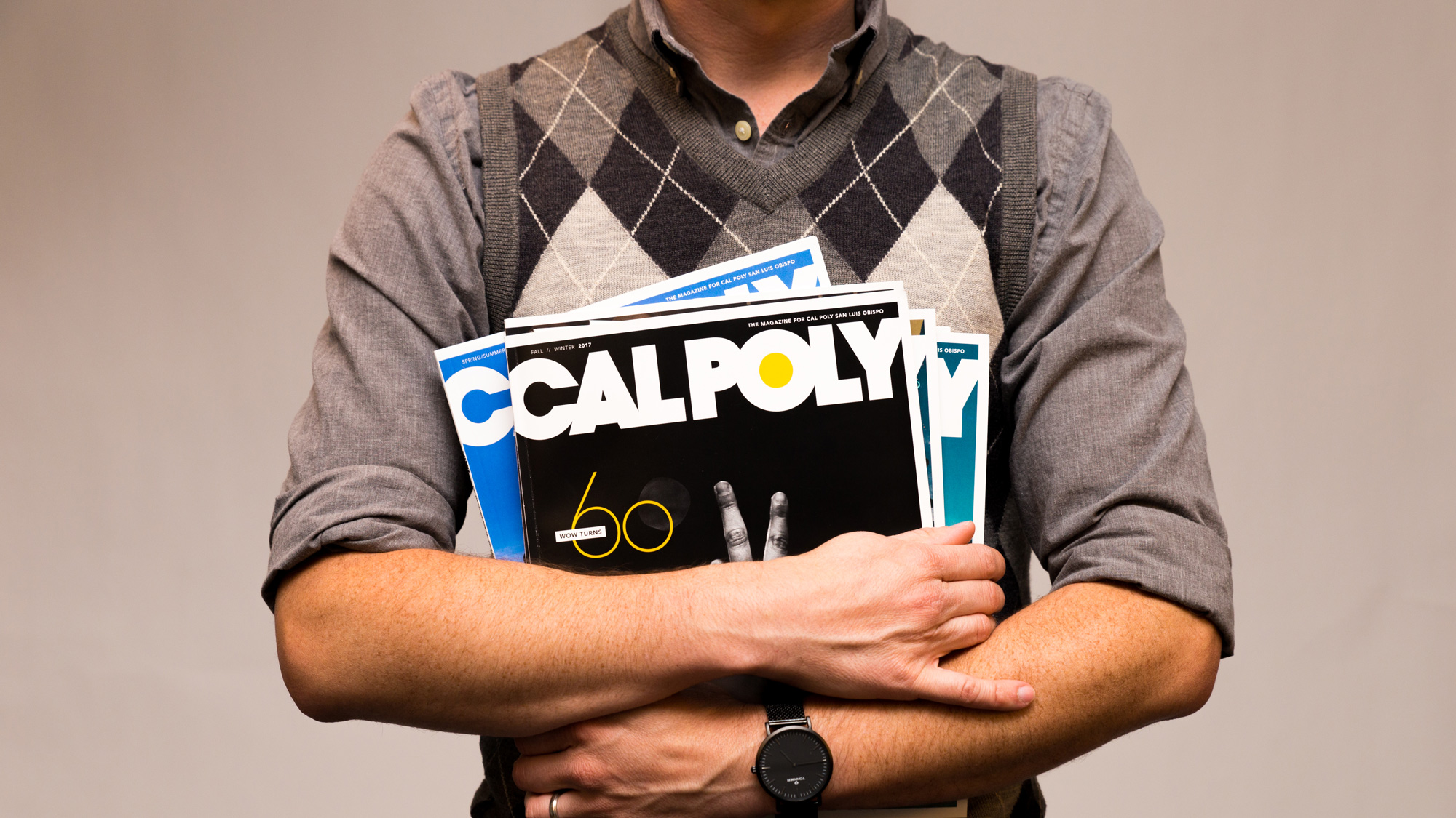 A man in a grey shirt holds a stack of Cal Poly Magazine copies