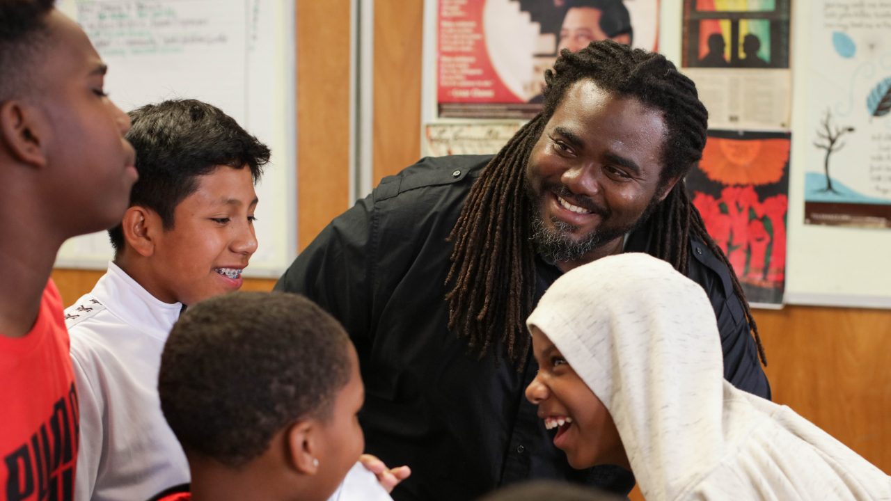 A man smiles at a group of laughing middle school boys