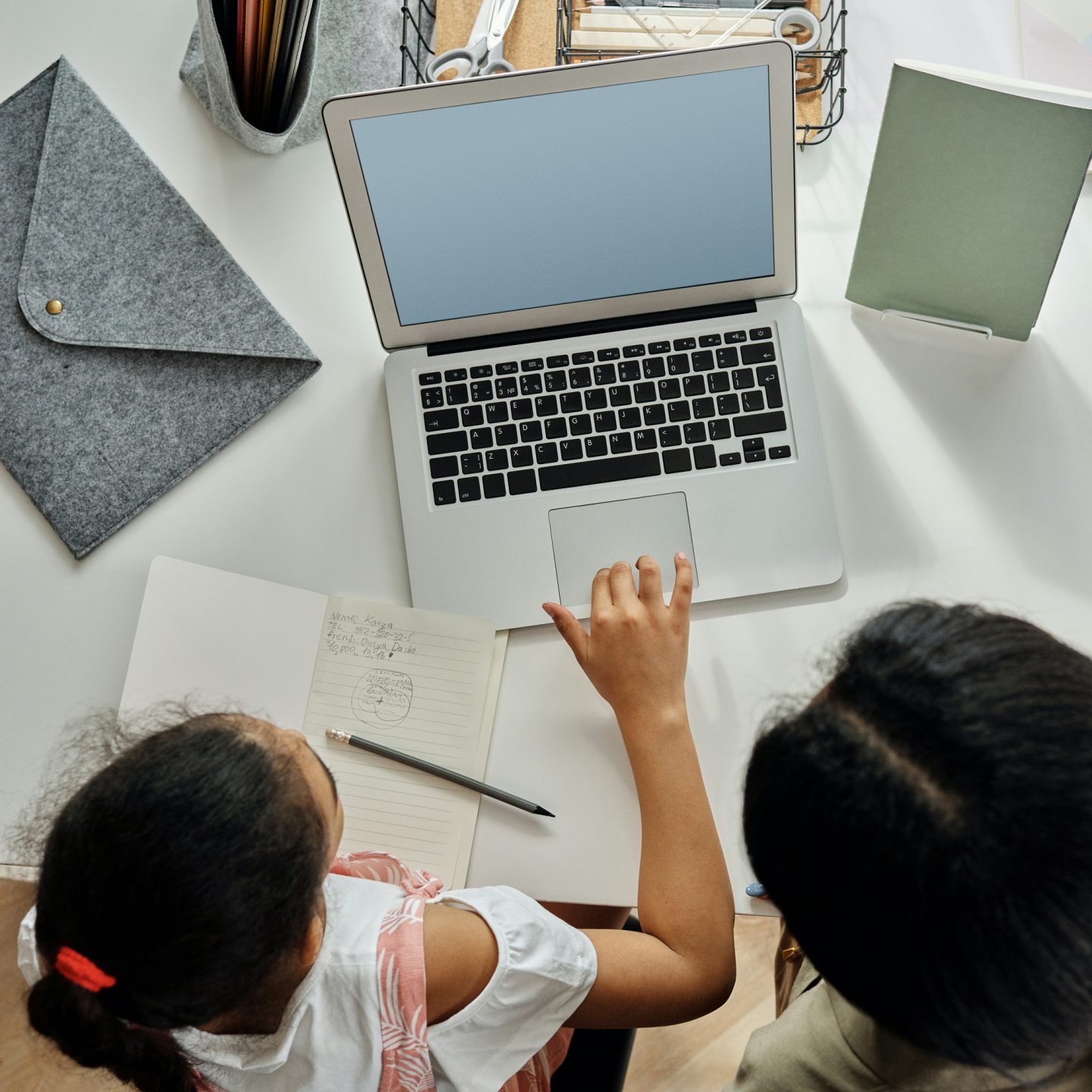 A child and a woman sit in front of a laptop on a white desk