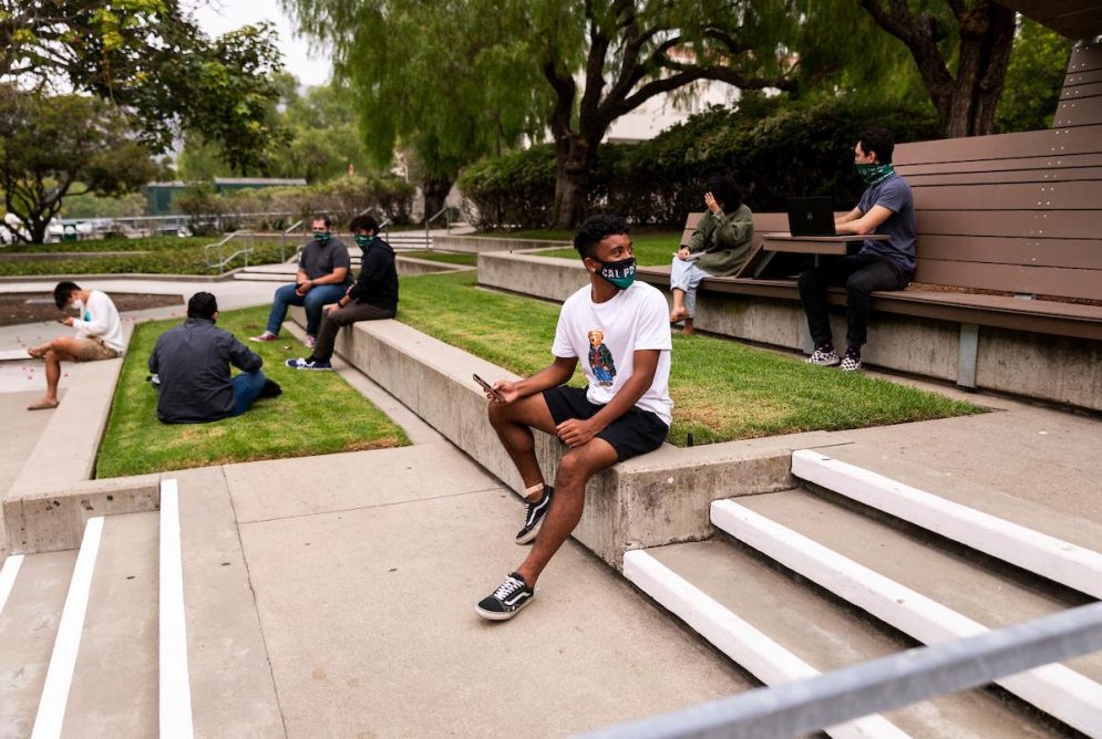 Students wearing face coverings sit on the steps in front of Kennedy Library.