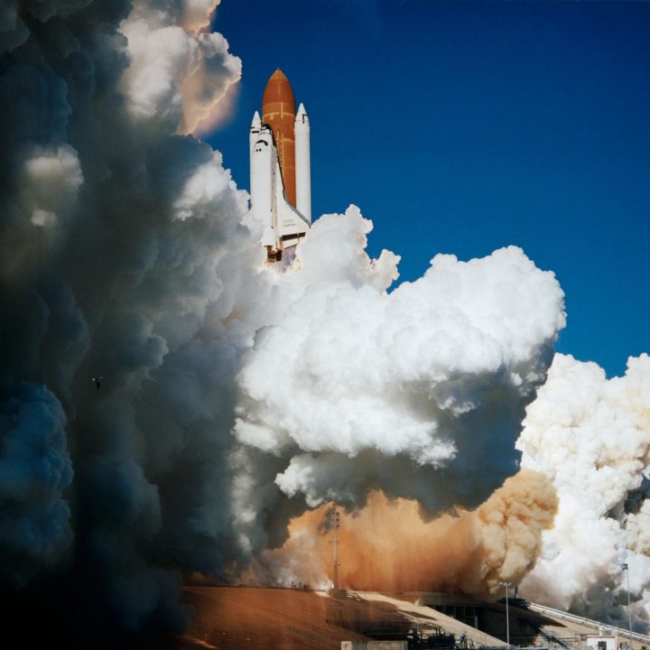 The Space Shuttle Challenger lifts off from Earth surrounded by steam