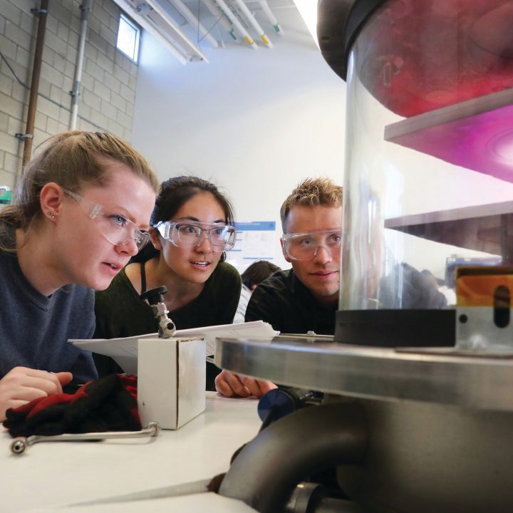 Three students wear safety goggles as they observe an experiment