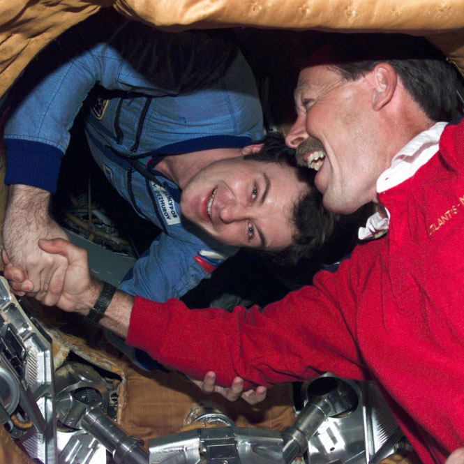 Two astronauts smile as they shake hands in the Space Shuttle
