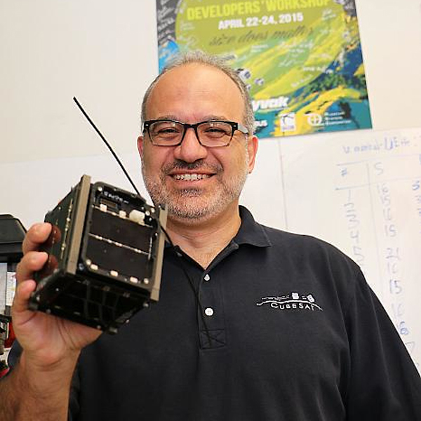 A man in a black shirt smiles as he holds a small satellite