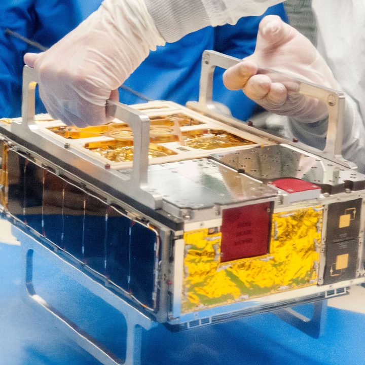 An engineer wearing globes holds a cubesat