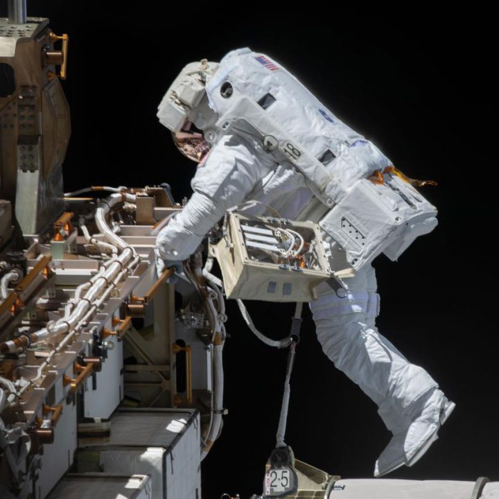 An astronaut in a white spacesuit performs a spacewalk outside the International Space Station