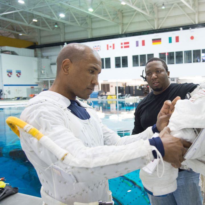 Two men inspect a NASA space suit in front of a pool