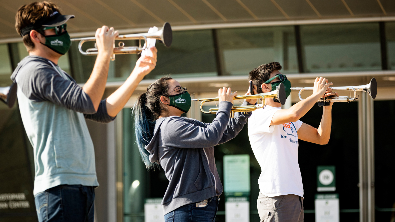 Three musicians play trumpet wearing face coverings and using filtration materials on bell covers