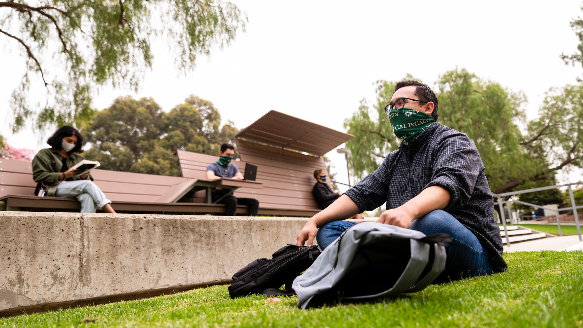 Four students sit on grass and benches wearing masks
