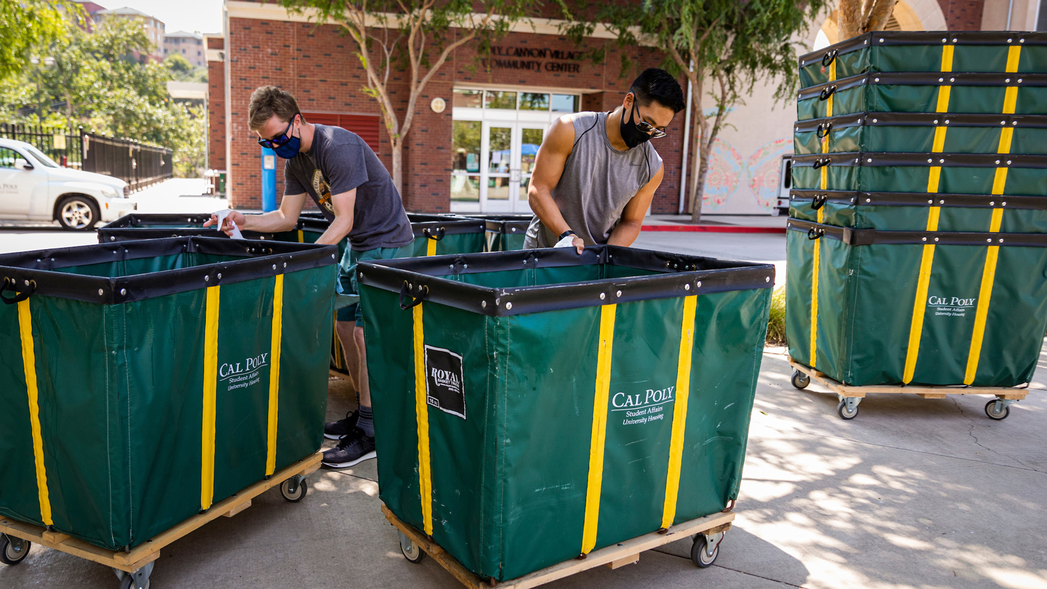 Two people disinfect green carts at Cal Poly's move in