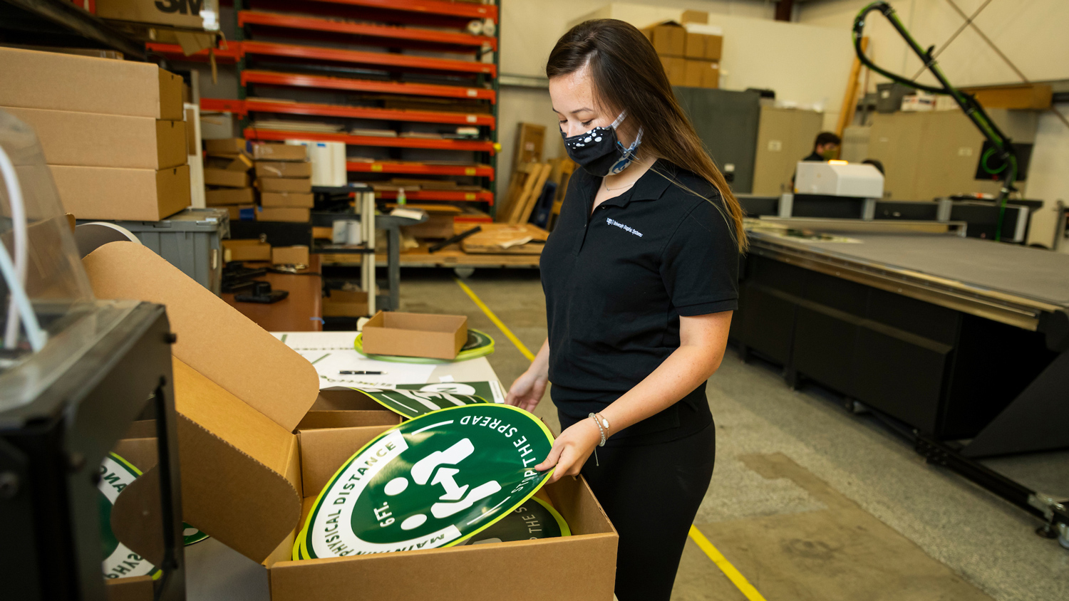 A woman wearing a mask puts a green sign into a cardboard box