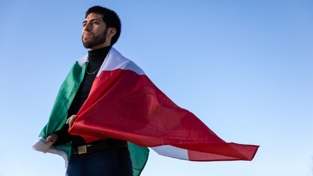 A man stands with the Mexican flag draped over his shoulders