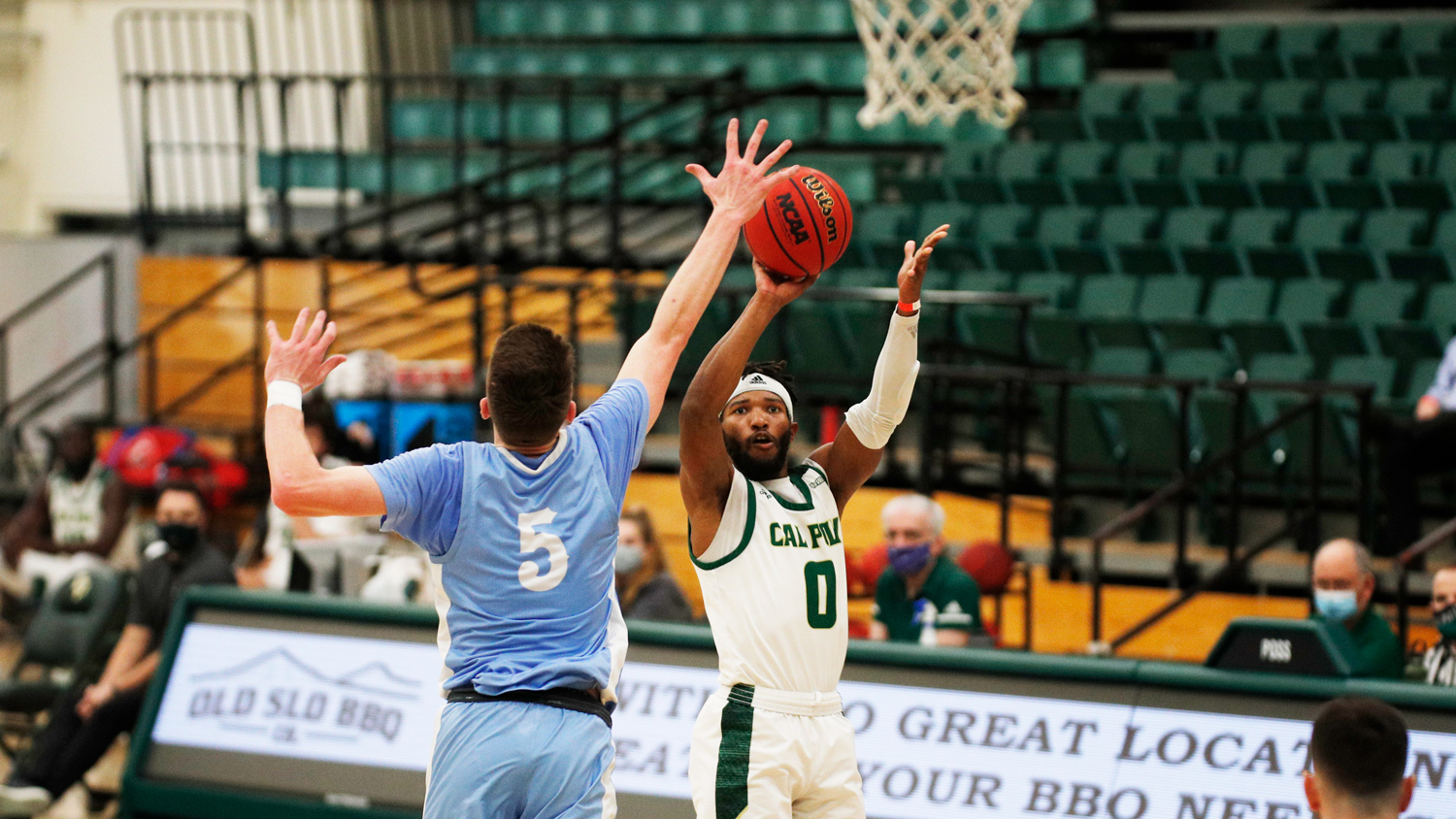 A basketball player shoots toward the basket over a defender wearing a blue jersey