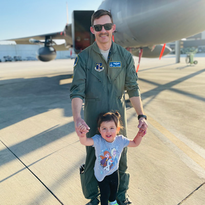 Jamie Hastings stands with his child in front of a fighter jet