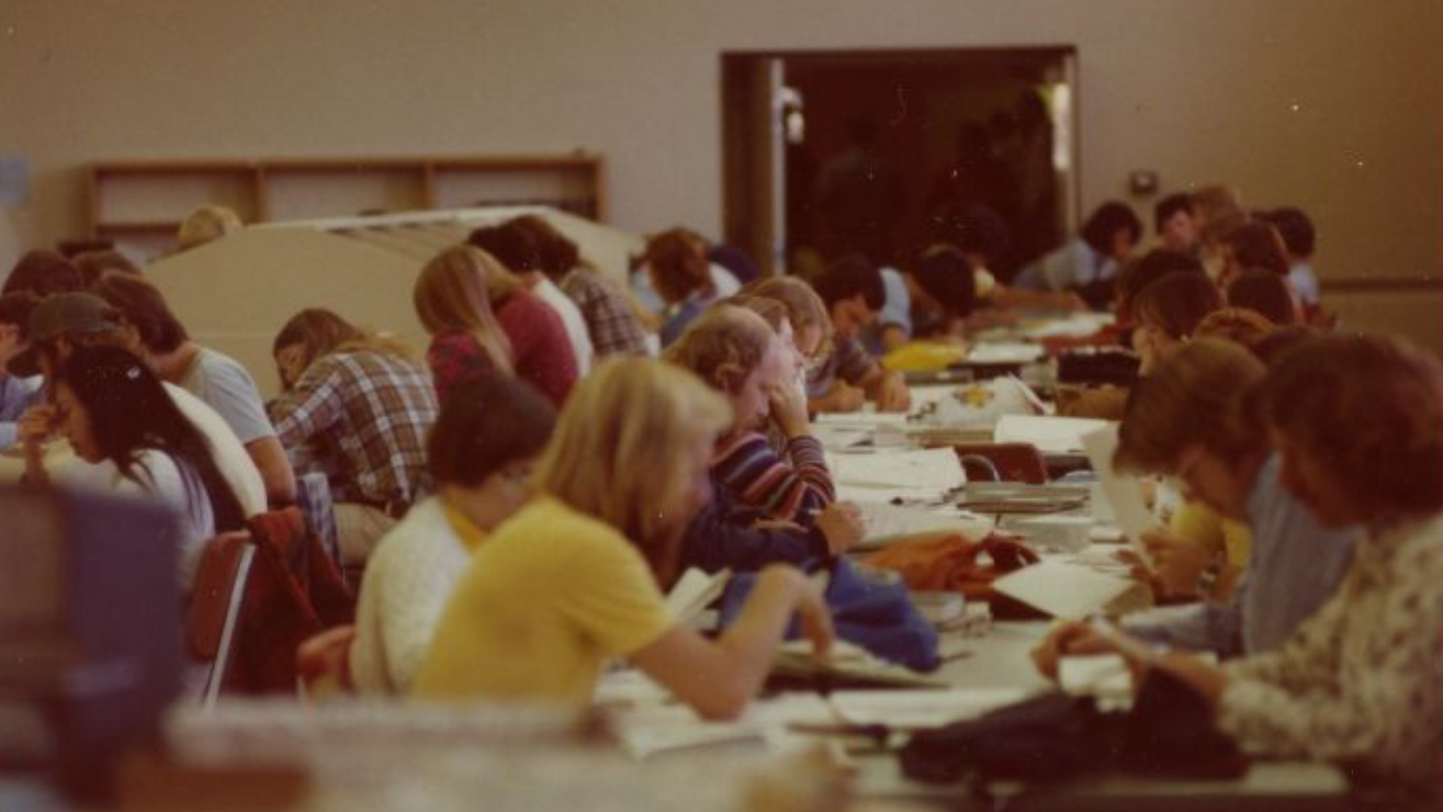 Students crowd around tables studying in a grainy photo from 1976