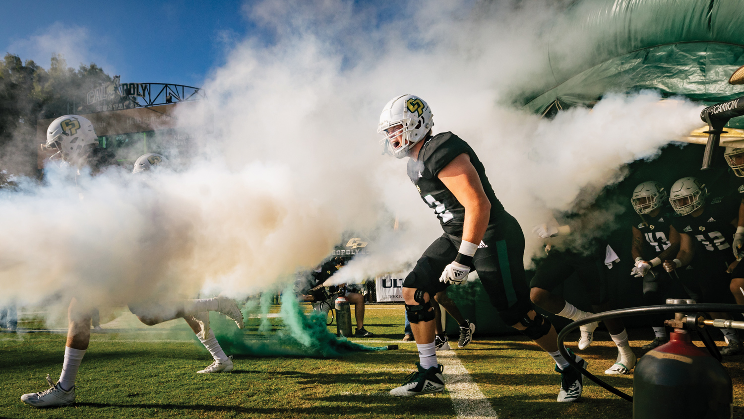 A football player runs out of a tunnel with smoke surrounding him