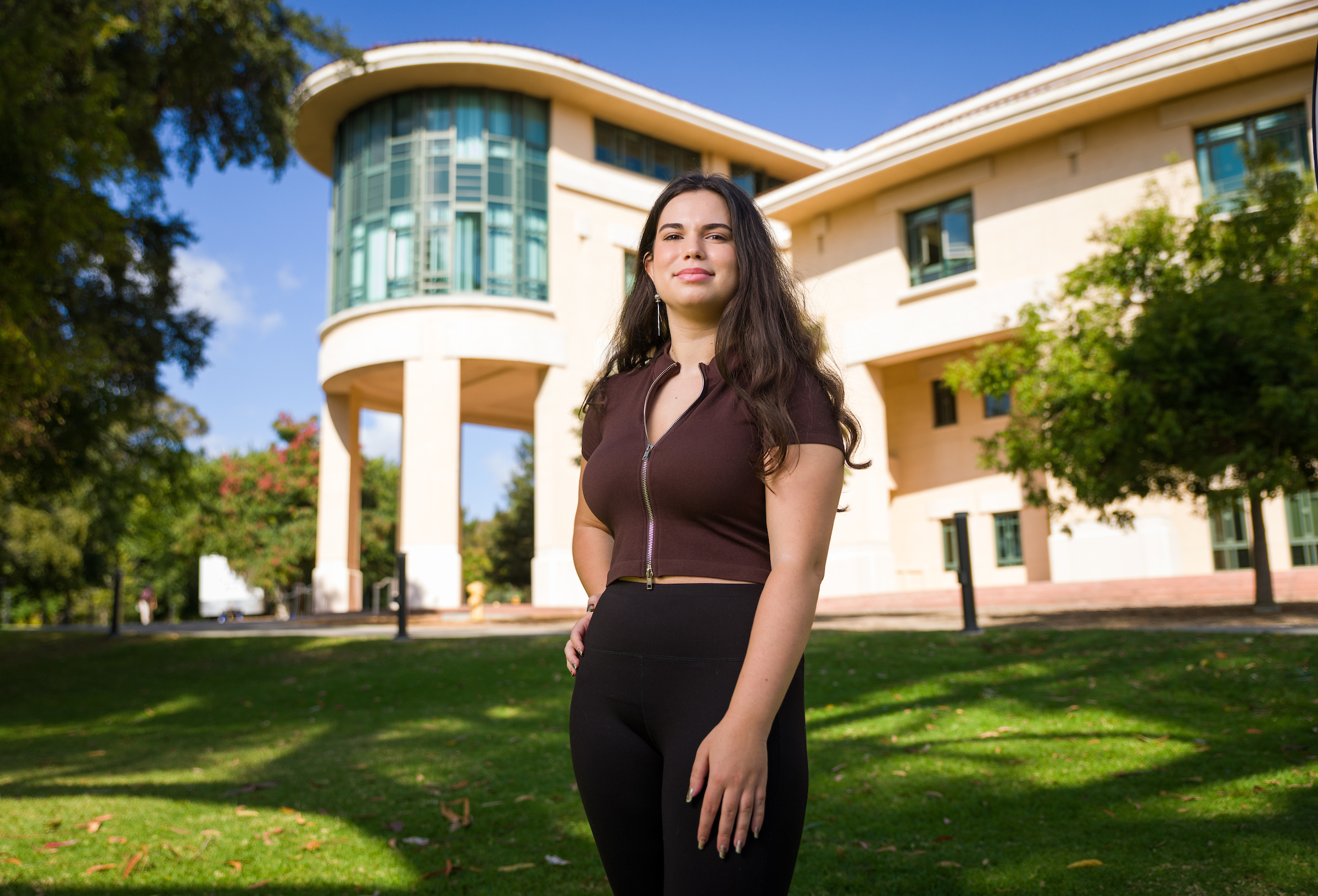 A young woman stands smiling in front of the Orfalea College of Business