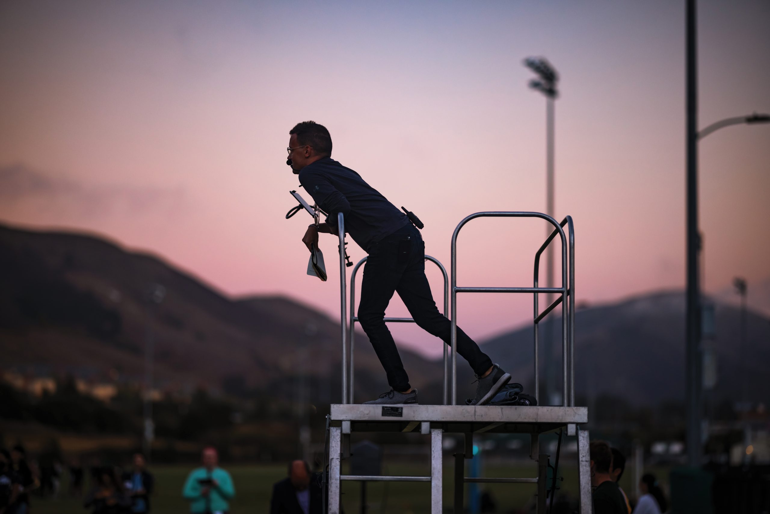 Silhouetted against the sunrise, band director Nick Waldron stands on a riser at the Mustang Band below