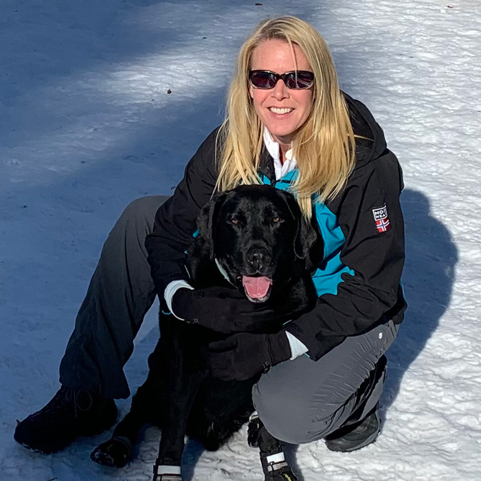 Kris Mitchell sits in the snow with a black laborador retriever