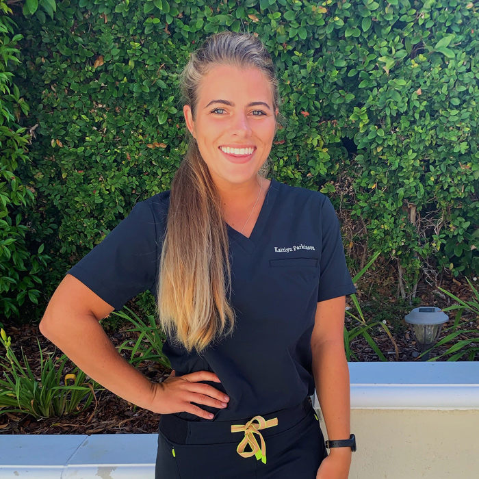 Katie Parkinson wears scrubs and stands in front of greenery