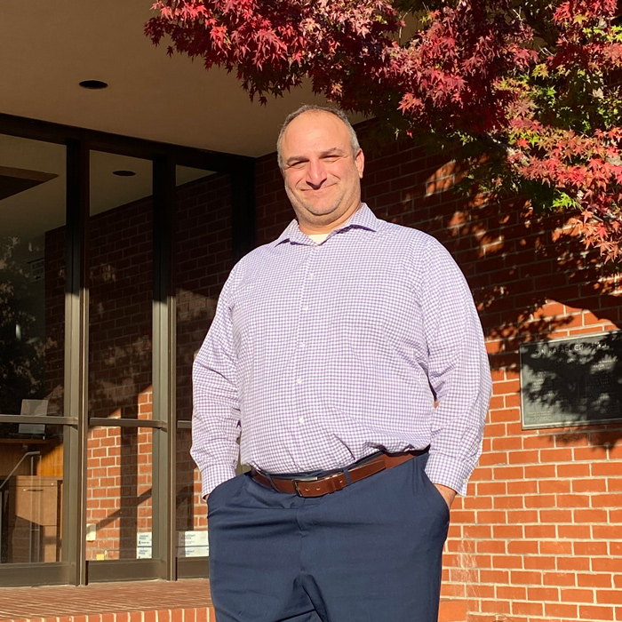 Raffi Boloyan stands in front of a brick wall and a tree