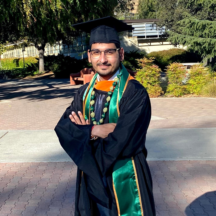 Anjaneya Teja Sarma Kalvakolanu stands with arms folded wearing graduation regalia