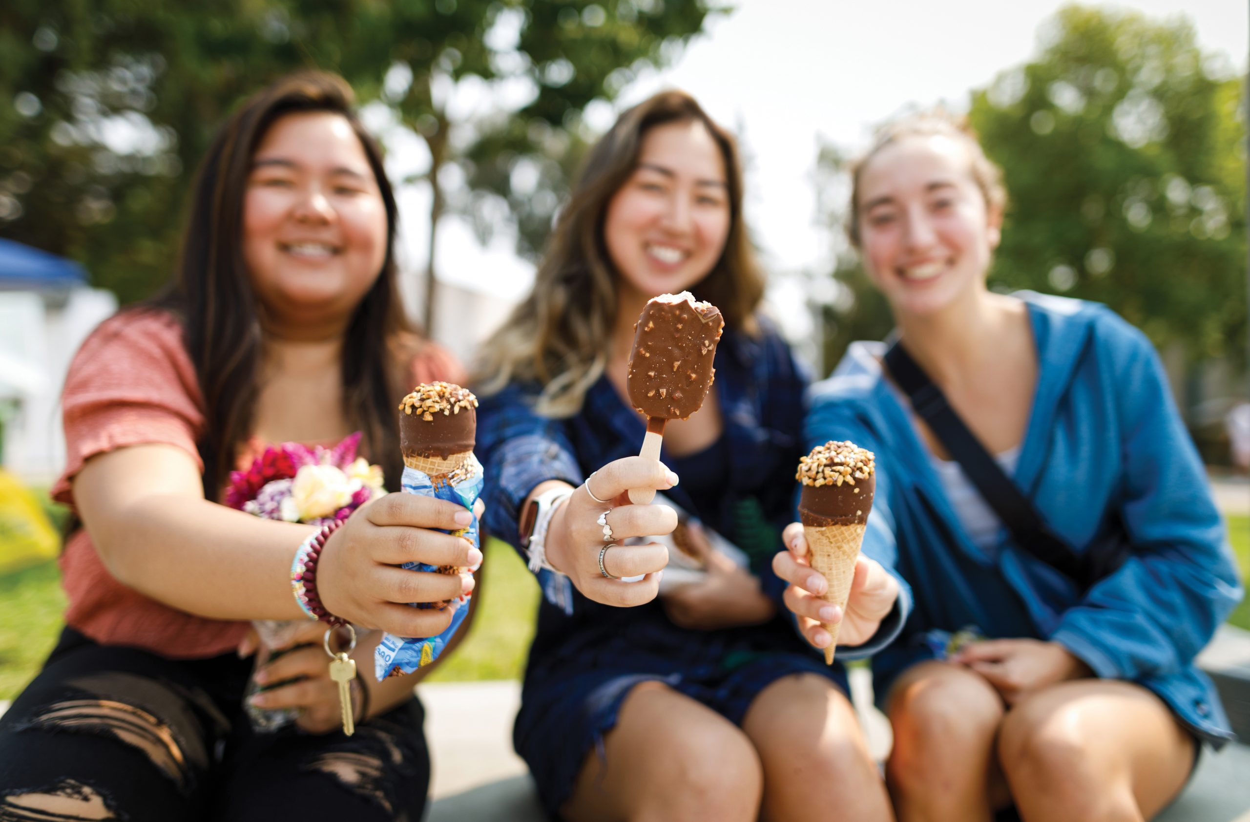 Three young women smile for the camera as they hold ice cream bars out in front of them