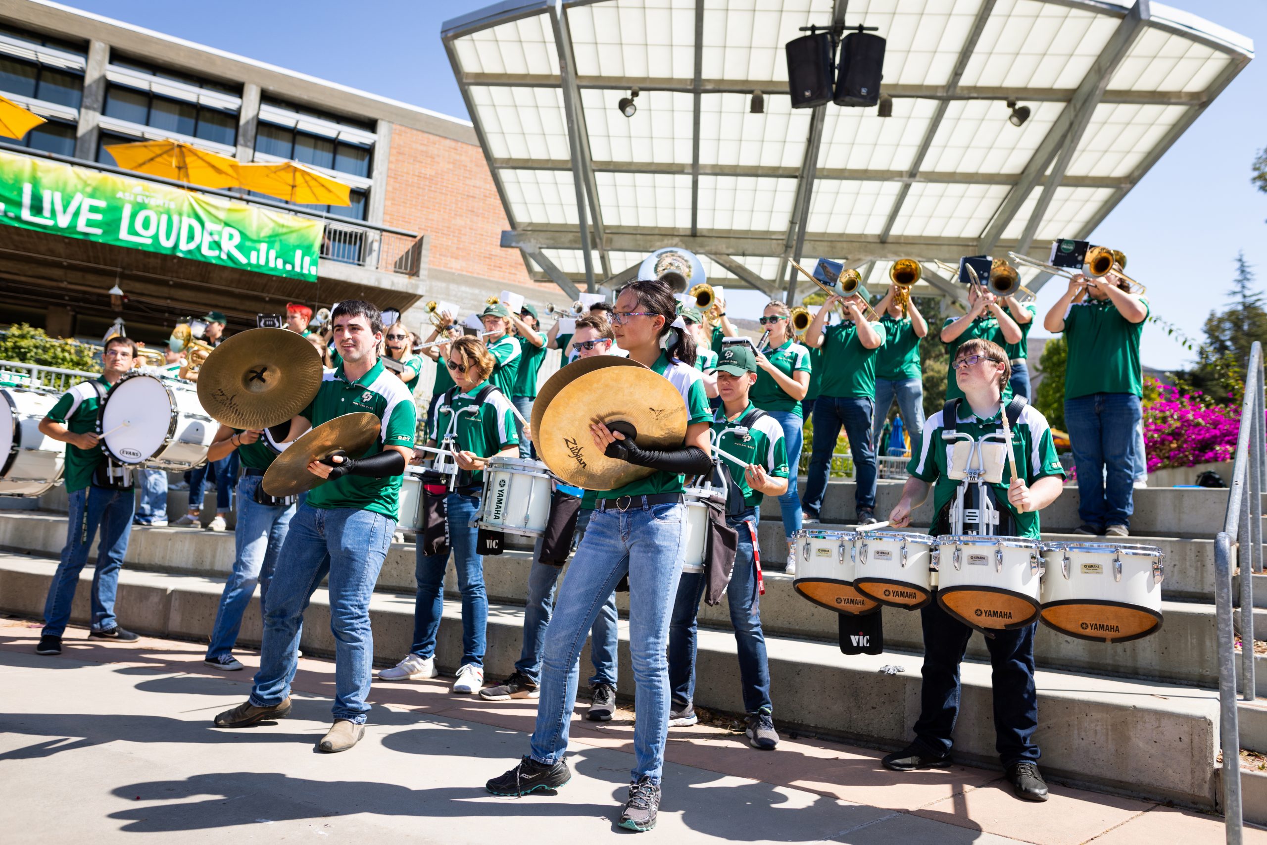 Members of the Mustang Band play drums, cymbals and horns on a set of wide concrete steps the University Union courtyard