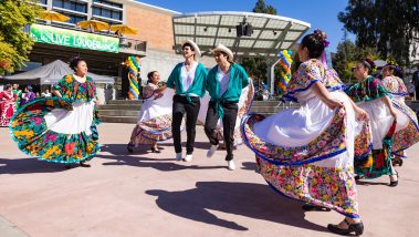 Seven men and women in traditional Mexican clothing dance in UU plaza
