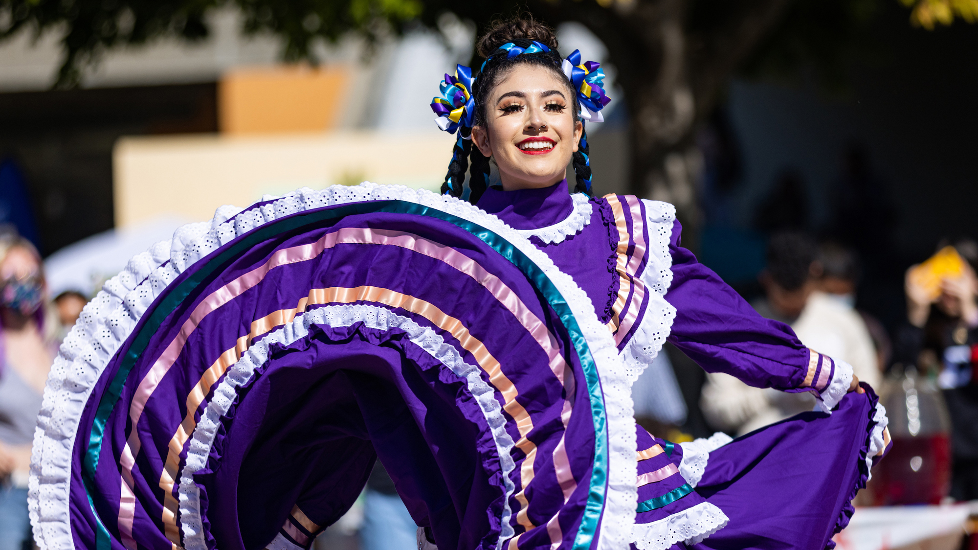 A woman in a bright purple dress smiles while dancing a traditional Mexican dance